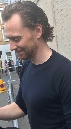 a man with long hair is looking at his cell phone while standing on the street