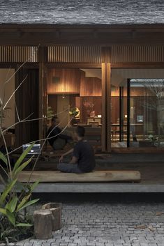 a man sitting on top of a wooden bench next to a tree in front of a building