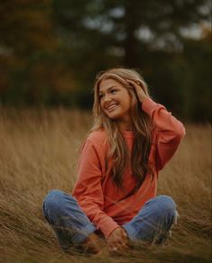 a woman sitting in the grass smiling and looking at the camera with her hands behind her head