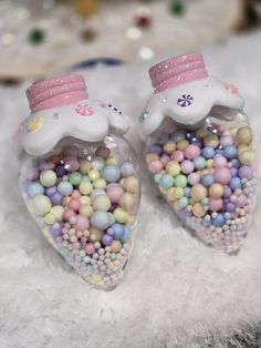 two glass heart shaped ornaments with candy in the shape of unicorns on top of them