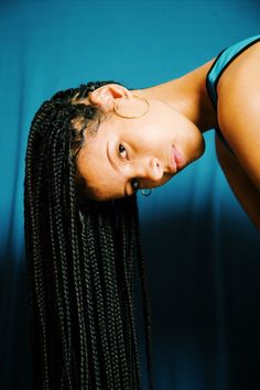 a woman with long braids is posing for the camera in front of a blue background