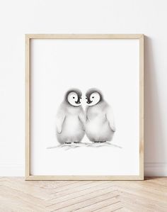 two little penguins are standing next to each other in front of a white wall and wooden frame