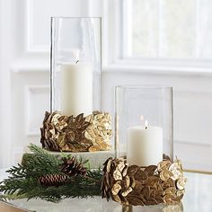 two glass vases filled with pine cones and candles