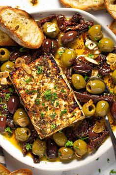 a white bowl filled with olives, bread and fish on top of a table