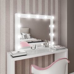 a white vanity table with a mirror and lights on the wall next to a chair