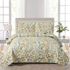 a bed with yellow flowers on it in a room next to two lamps and windows