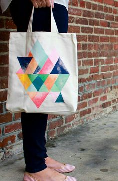 a woman is holding a colorful tote bag on her feet while standing in front of a brick wall