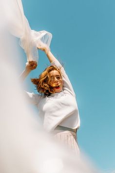 a woman in white shirt and skirt holding up a plastic bag over her head with blue sky background