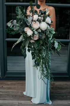 a woman holding a bouquet of flowers in front of a glass door with greenery