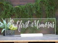 a clear acrylic sign sitting on top of a wooden table next to a potted plant