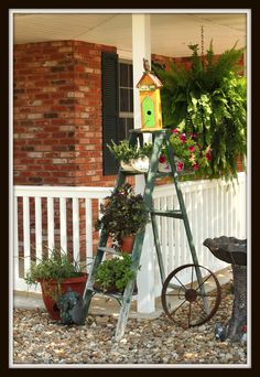 a birdhouse is sitting on top of a ladder next to some flowers and potted plants