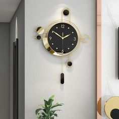 a black and gold clock hanging on the wall next to a potted green plant