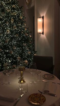 a christmas tree is lit up in the corner of a room with white table cloths and place settings