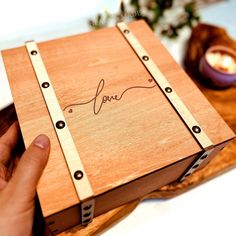 a person holding a wooden box with the word love written on it and two candles in the background