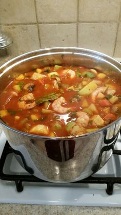 a pot filled with shrimp and vegetables on top of a gas burner in a kitchen