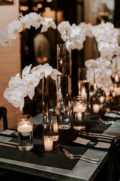 a table with candles and vases filled with white flowers on top of each other