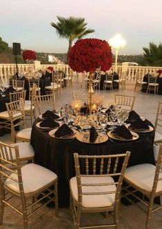 a table set up with black and white linens, gold chargers and red roses