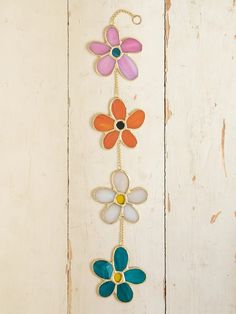 three colorful flowers hanging from a chain on a white wooden wall with paint chippings