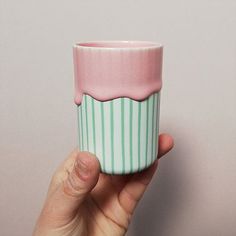 a hand holding a pink and green striped cup with frosting on the rims