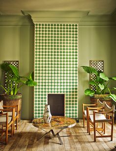 a living room with green walls and wooden flooring, potted plants on either side of the fireplace