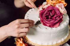 two people are decorating a white cake with pink and orange flowers