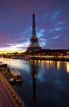 the eiffel tower is lit up at night with cars passing by in front