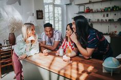 four people sitting at a bar laughing and drinking