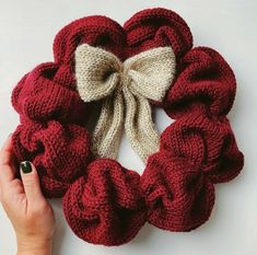 a hand holding a red and white knitted scrunffle with a bow on it