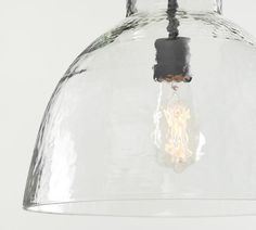 a clear glass pendant light hanging from a ceiling fixture with a bulb on the end