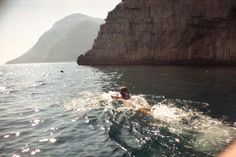 a person swimming in the ocean next to a cliff