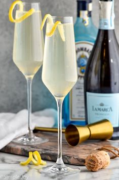 two champagne glasses with lemon garnish sit next to bottles and corks