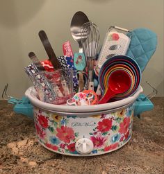 a flowered pot filled with kitchen utensils