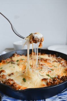 a fork is lifting some lasagna out of a skillet with meat and cheese