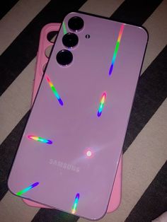 the back of a pink phone case with rainbow stickers on it, sitting on a black and white striped surface