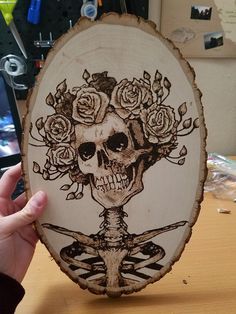 a person holding up a piece of wood with a skull and roses on it