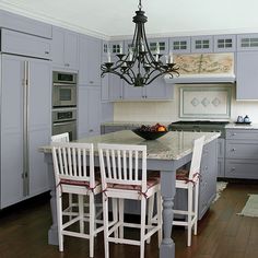 a large kitchen with white cabinets and wooden floors is pictured in this image, there are four chairs at the center of the table