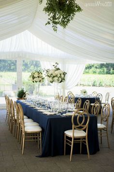 a table set up for an event with white flowers and greenery on the tables