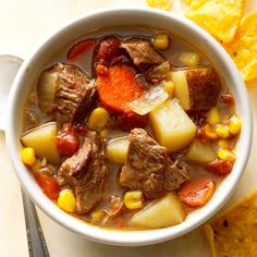 a white bowl filled with beef and potatoes next to tortilla chips on a table