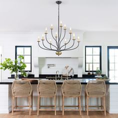 a chandelier hangs over a kitchen island with four wicker chairs in front of it