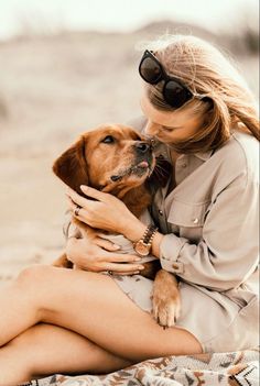 a woman is sitting on the beach with her dog and kissing her nose while wearing sunglasses