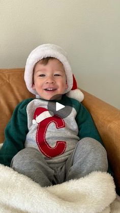 a young boy sitting on top of a brown couch wearing a santa hat and smiling