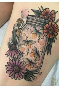 a woman's thigh with flowers and a mason jar tattoo on her leg,