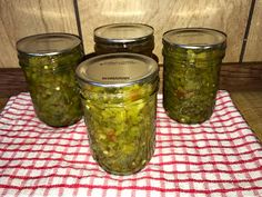 four jars filled with pickles sitting on top of a red and white checkered table cloth