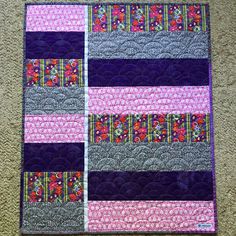 a purple and pink quilted wall hanging on the floor next to a brown carpet