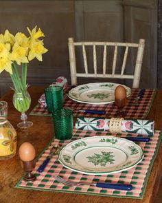 a wooden table topped with plates and vases filled with yellow daffodils