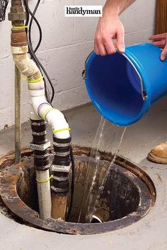 a man is pouring water from a blue bucket into a hole in the ground with pipes