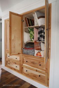 an open wooden cabinet with pillows and blankets