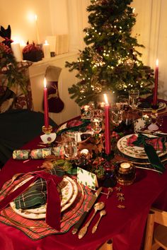 a christmas table setting with candles, plates and napkins in front of a tree