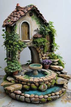 a small house with a fountain in front of it and plants growing on the roof