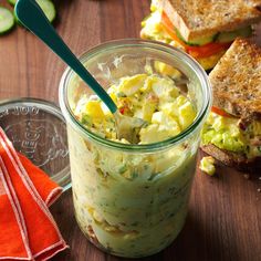 a glass jar filled with food sitting on top of a wooden table next to slices of bread